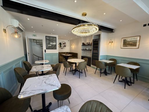 Intérieur d'un café moderne avec tables en marbre et chaises vertes, éclairage élégant.